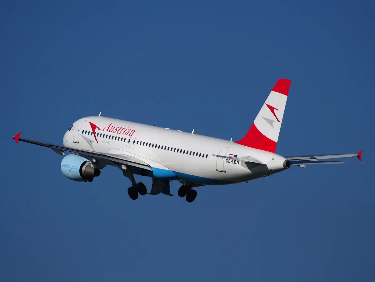 Um Airbus A320 da Austrian Airlines subindo após a decolagem contra um céu de azul intenso, com o trem de pouso ainda baixado.