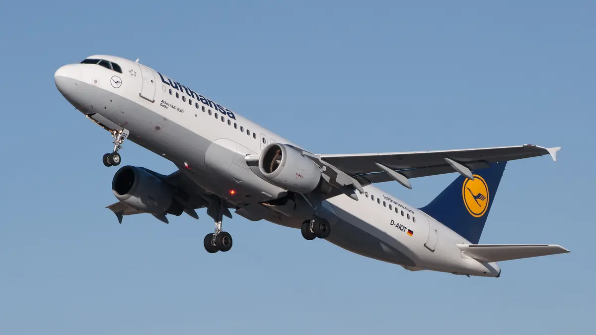 Um Airbus A320 da Lufthansa em subida acentuada após a decolagem, com o trem de pouso ainda estendido.