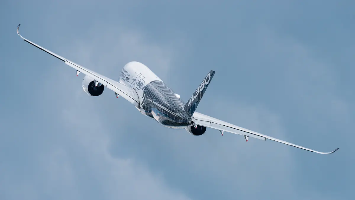Um Airbus A350 em curva inclinada durante o voo, contra um céu claro e enevoado, visto por trás e de lado.