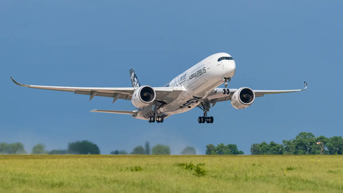 Um Airbus A350 decolando sobre um campo gramado sob um céu de azul intenso, com o trem de pouso ainda estendido.