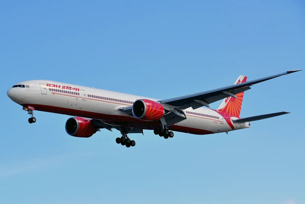 Um Boeing 777-300ER da Air India na aproximação contra um céu azul brilhante, com o trem de pouso estendido.